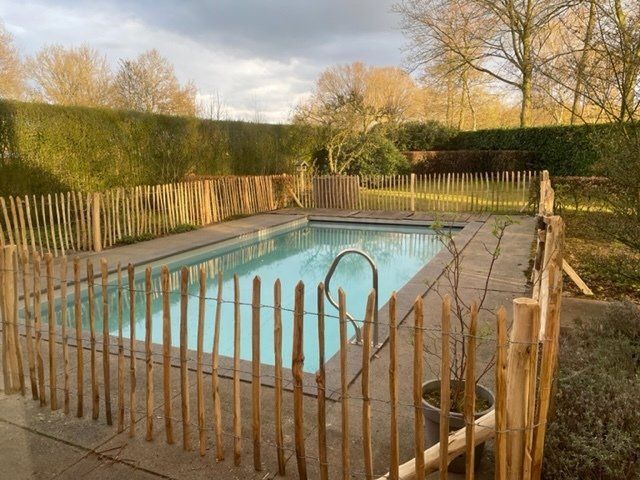 Een groot zwembad omgeven door een kastanje houten hek.