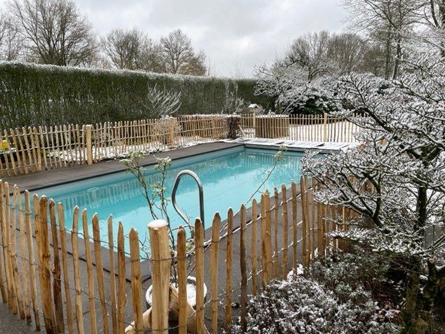 Een zwembad omgeven door een houten schapenhek op een besneeuwde dag.