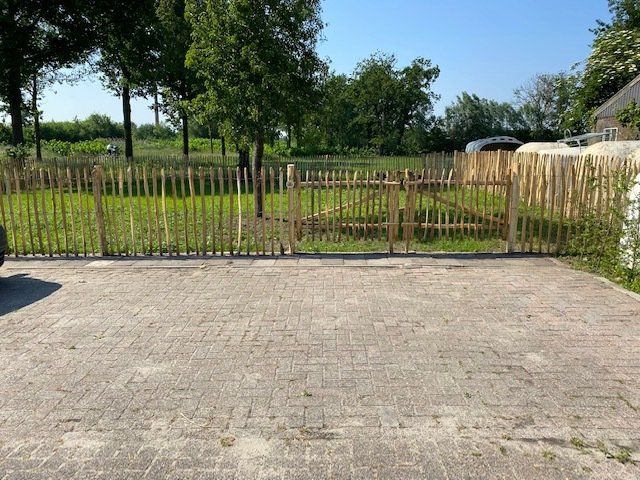 Een bakstenen oprit met een kastanje houten hekwerk op de achtergrond en een tuinpoort.