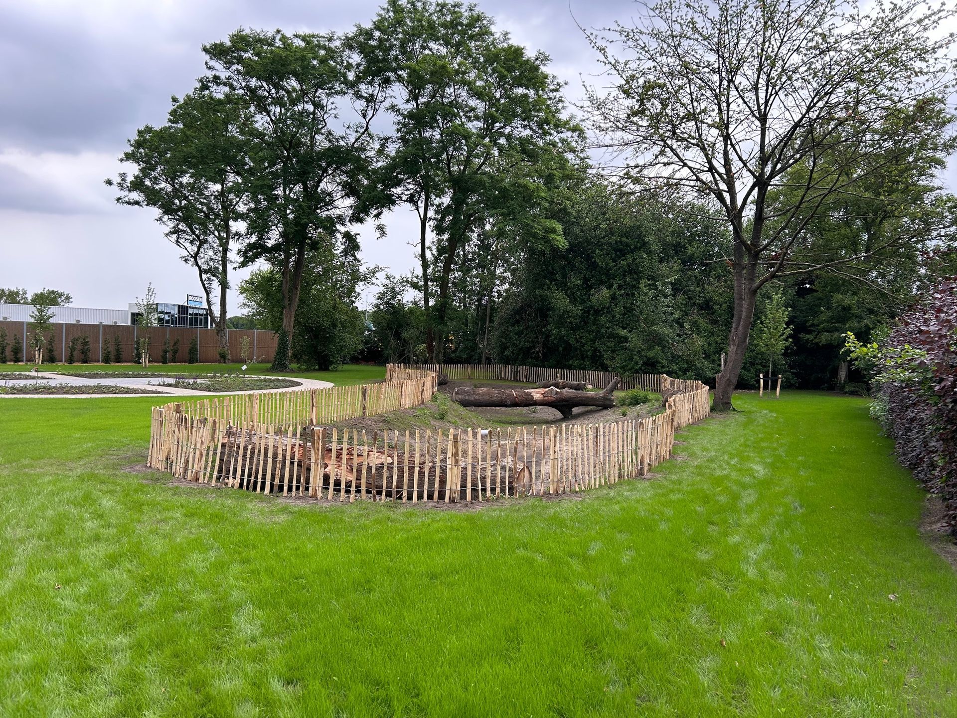Een houten hek omringt een weelderig groen veld met bomen op de achtergrond.