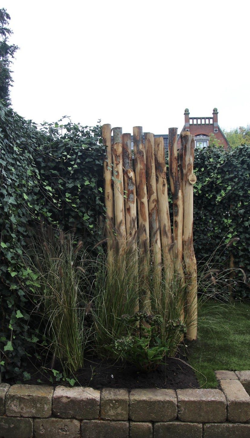 Een houten hek gemaakt van kastanje palen in een tuin met een huis op de achtergrond.