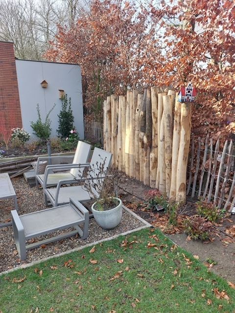 Een tuin met een kastanje palen wand, stoelen, tafels en potplanten.