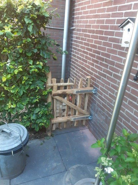 Een bakstenen muur met een klein kastanje tuinpoortje ervoor.