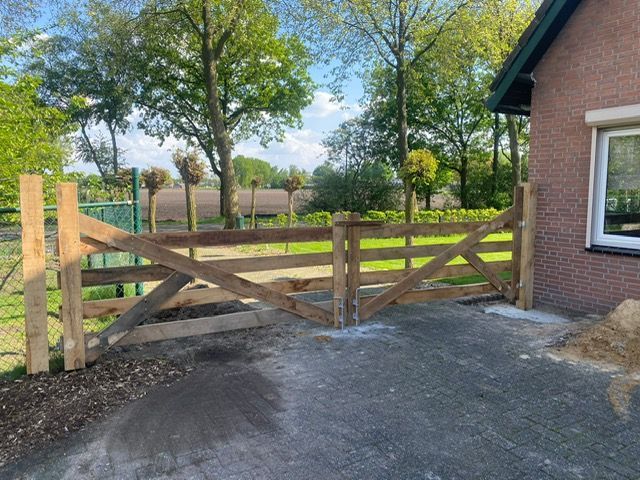Voor een bakstenen huis staat een houten robinia landhek.