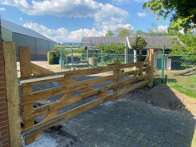 Voor een bakstenen gebouw staat een robinia landhek.