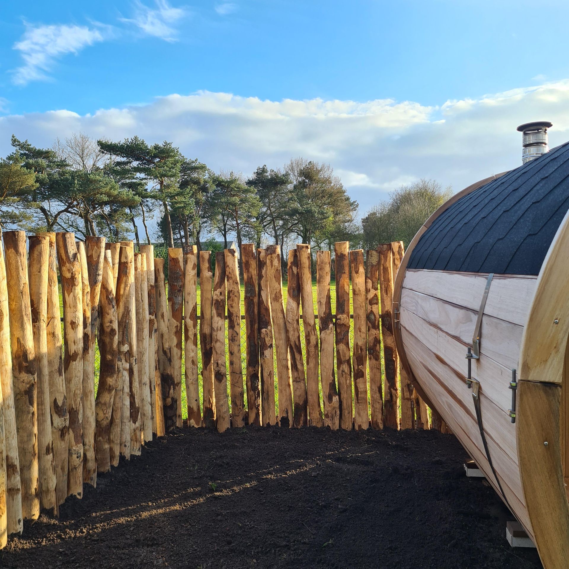 Een kastanje palenwand omringt een groot houten vat