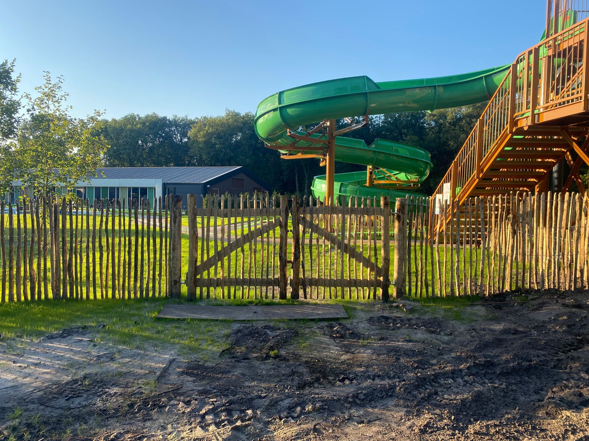 Achter een houten hek bevindt zich een groene waterglijbaan.