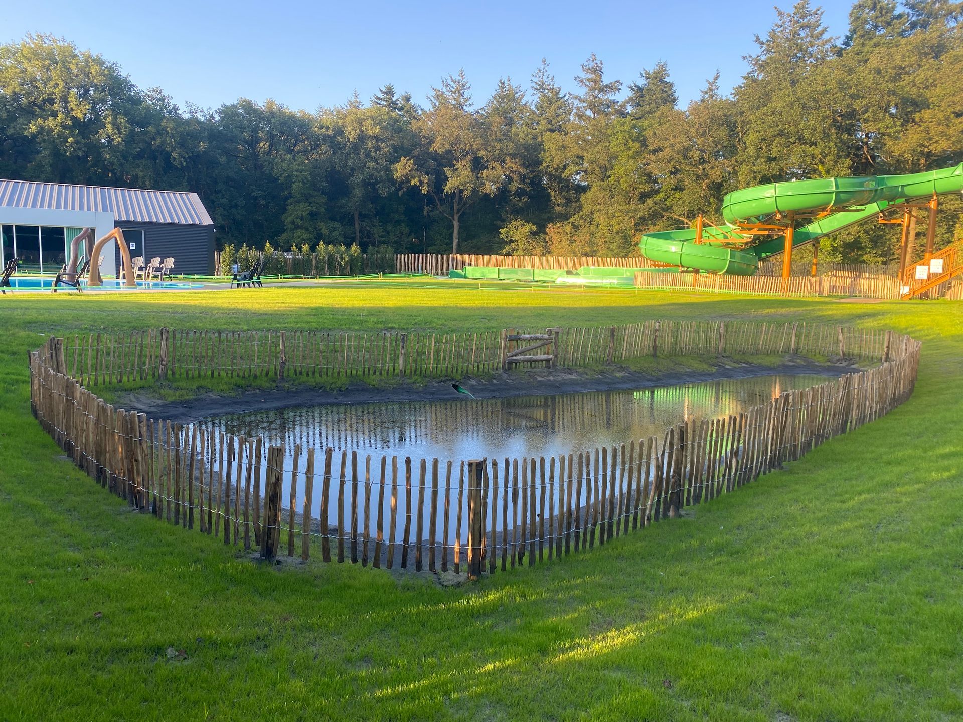 Een vijver met een houten hek eromheen en een waterglijbaan op de achtergrond.