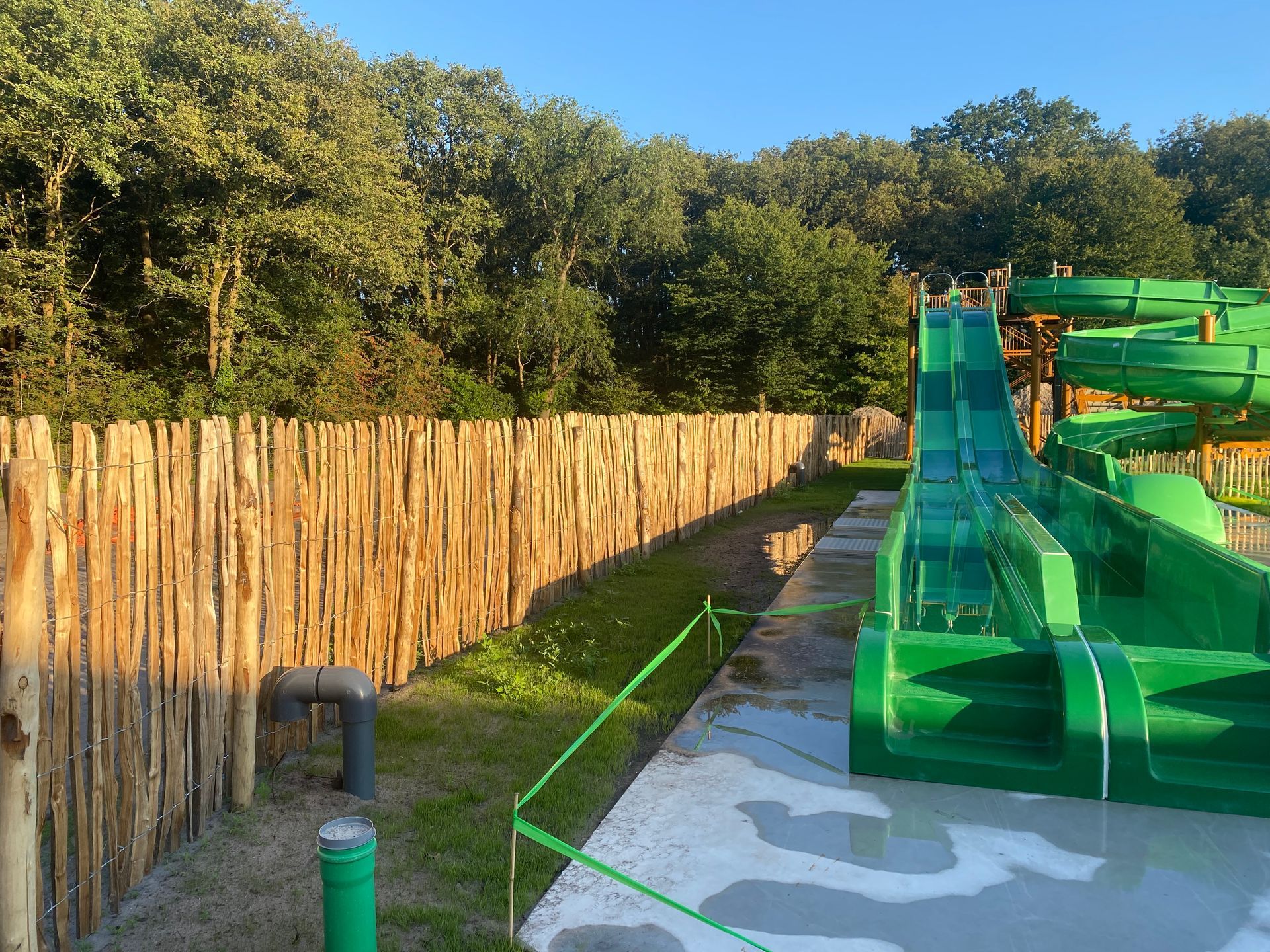 Een groene waterglijbaan met een houten hek op de achtergrond.