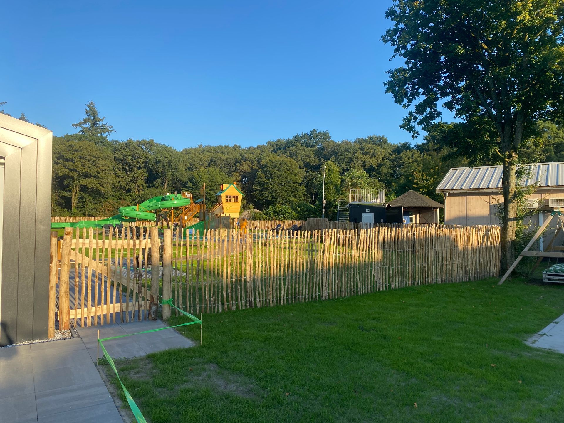 Een houten hek omringt een weelderig groen veld met een speeltuin op de achtergrond.