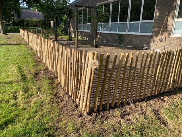 Een houten schapenhek omringt een grasveld voor een huis.