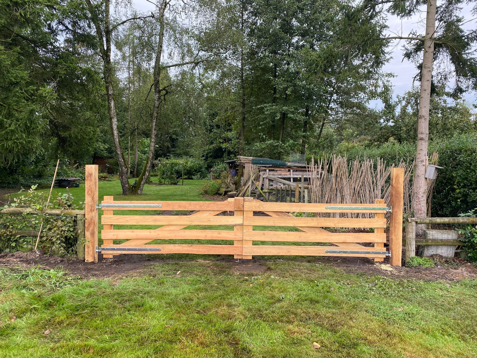 Houten poort in een grasveld, met een bosrijke achtergrond.