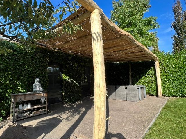 Midden in een tuin staat een houten pergola van robinia palen.
