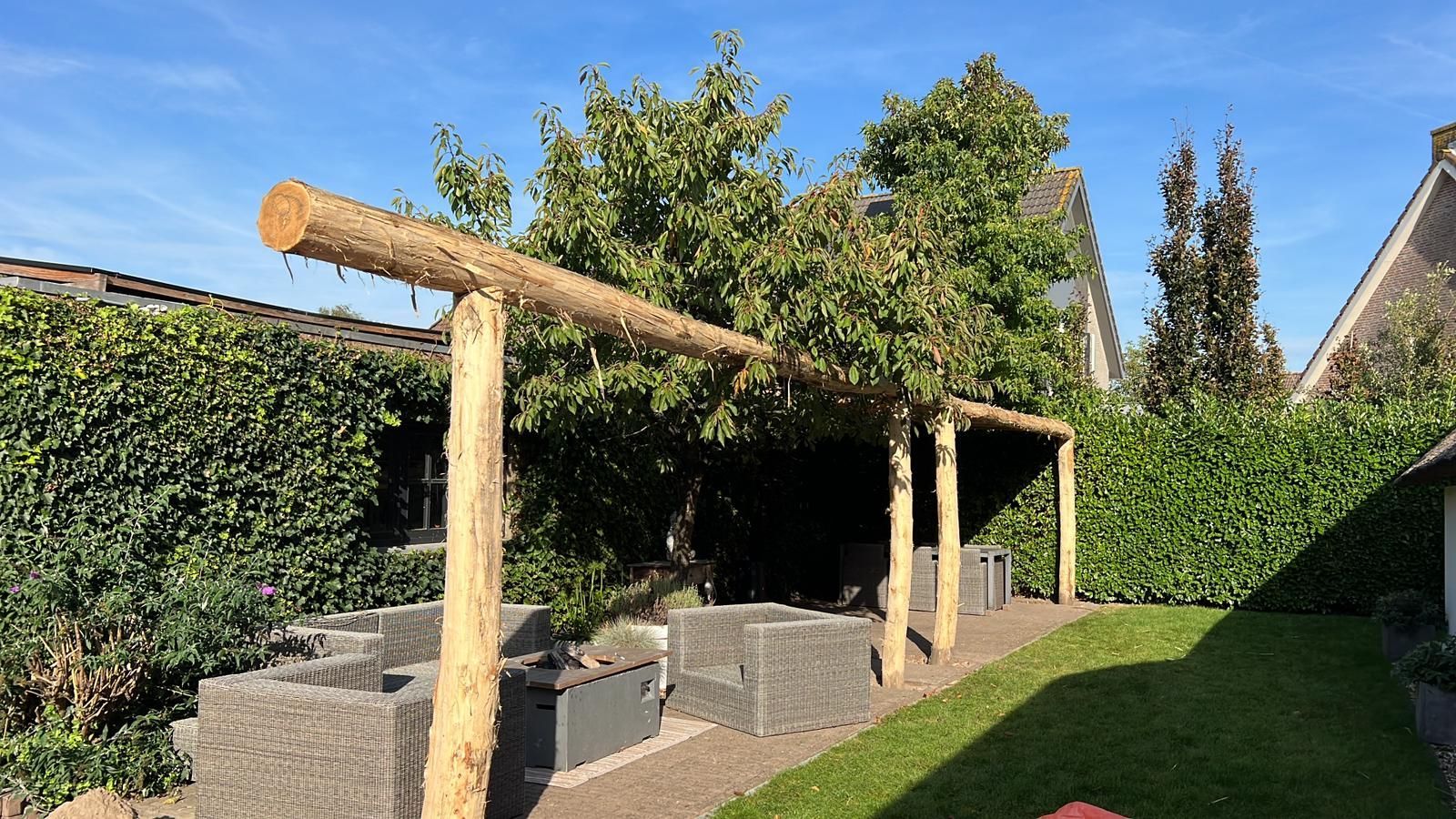 In de achtertuin van een huis wordt een houten pergola gebouwd van robinia palen.