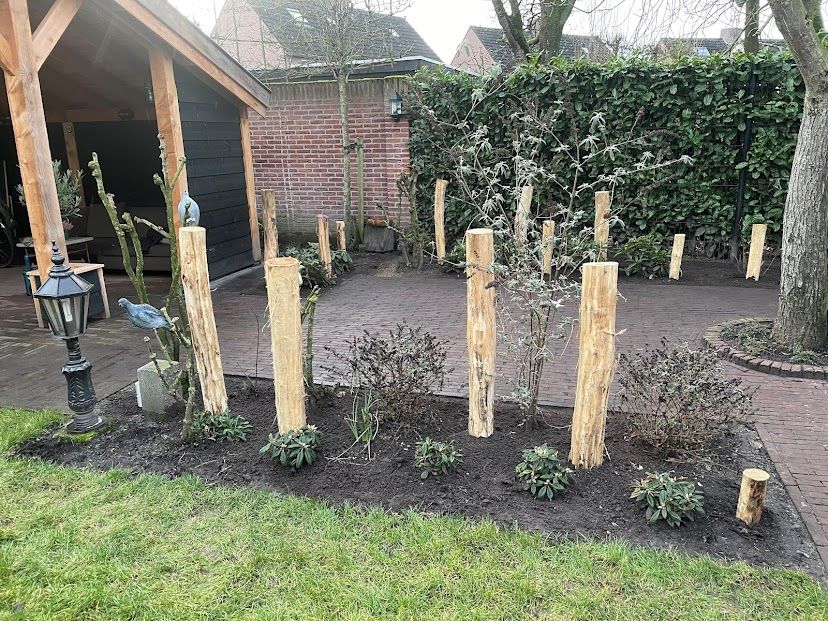 Een rij houten robinia palen in een tuin met een bakstenen gebouw op de achtergrond.