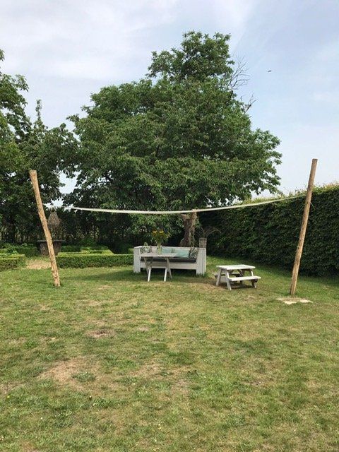 Een grasveld met een bank en een picknicktafel onder een afdak van robinia palen.