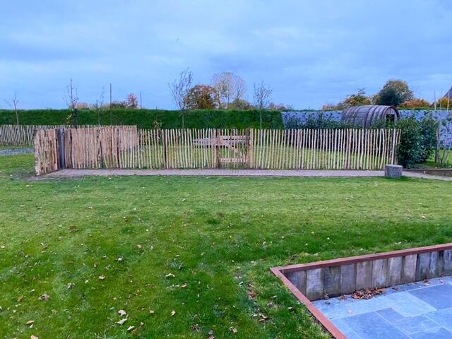 Midden in een weelderig groen veld staat een houten schapenhek van kastanjehout.