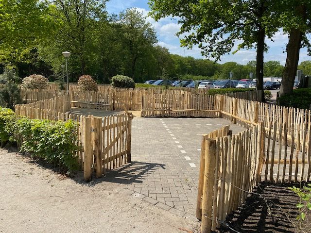 Een houten schapenhek omringt een parkeerplaats waar auto's geparkeerd staan.