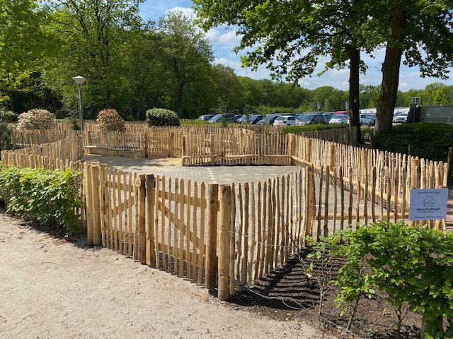 Een houten schapenhek met tuinpoortjes omringt een cirkelvormig gebied in een park.