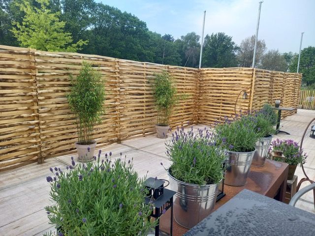 Een schutting van kastanje vlechtschermen met potplanten ervoor.