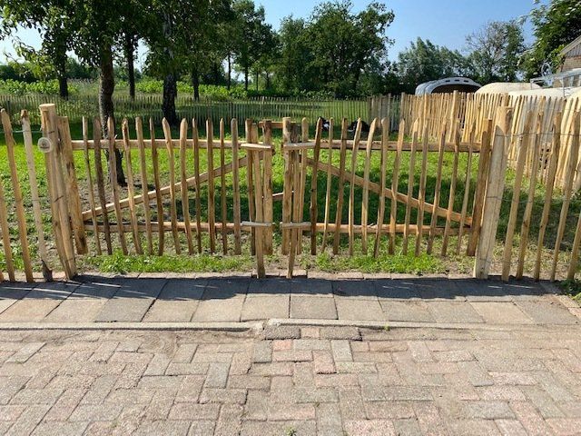 Op een stenen oprit staat een kastanje houten hek met een tuinpoort.