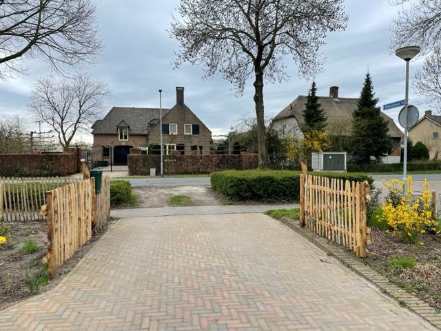 Een stenen oprit met een kastanje tuinpoort dat naar een huis leidt.