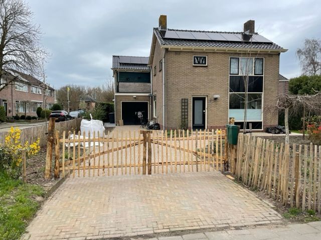 Een huis met een kastanje tuinpoort ervoor.