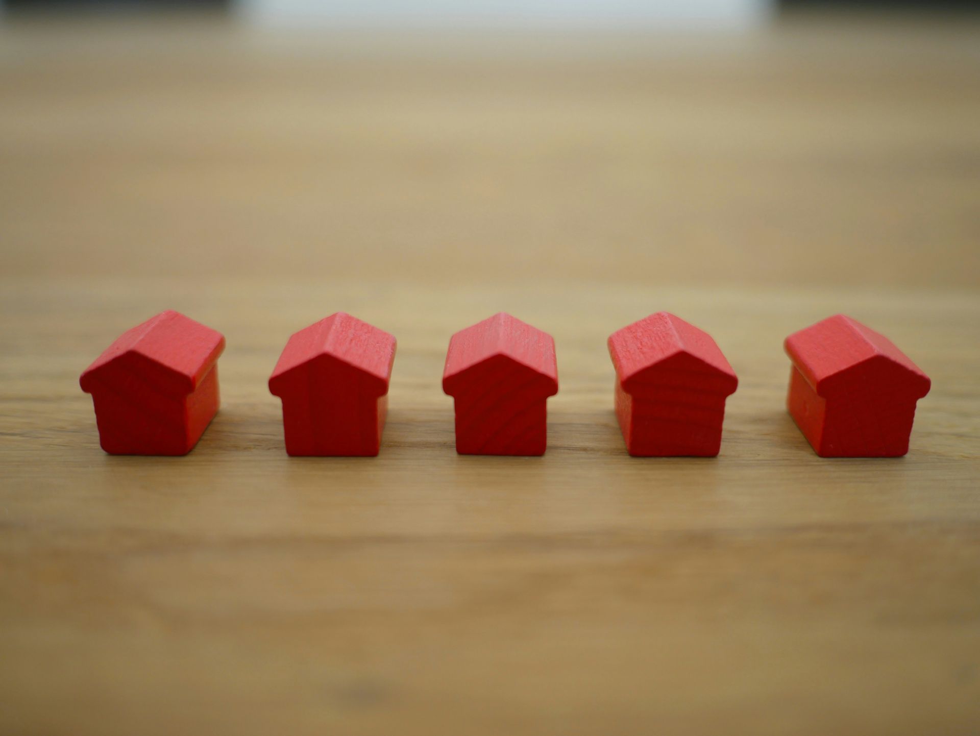 This image shows a line of five small red house-shaped pieces arranged in a row on a wooden surface.
