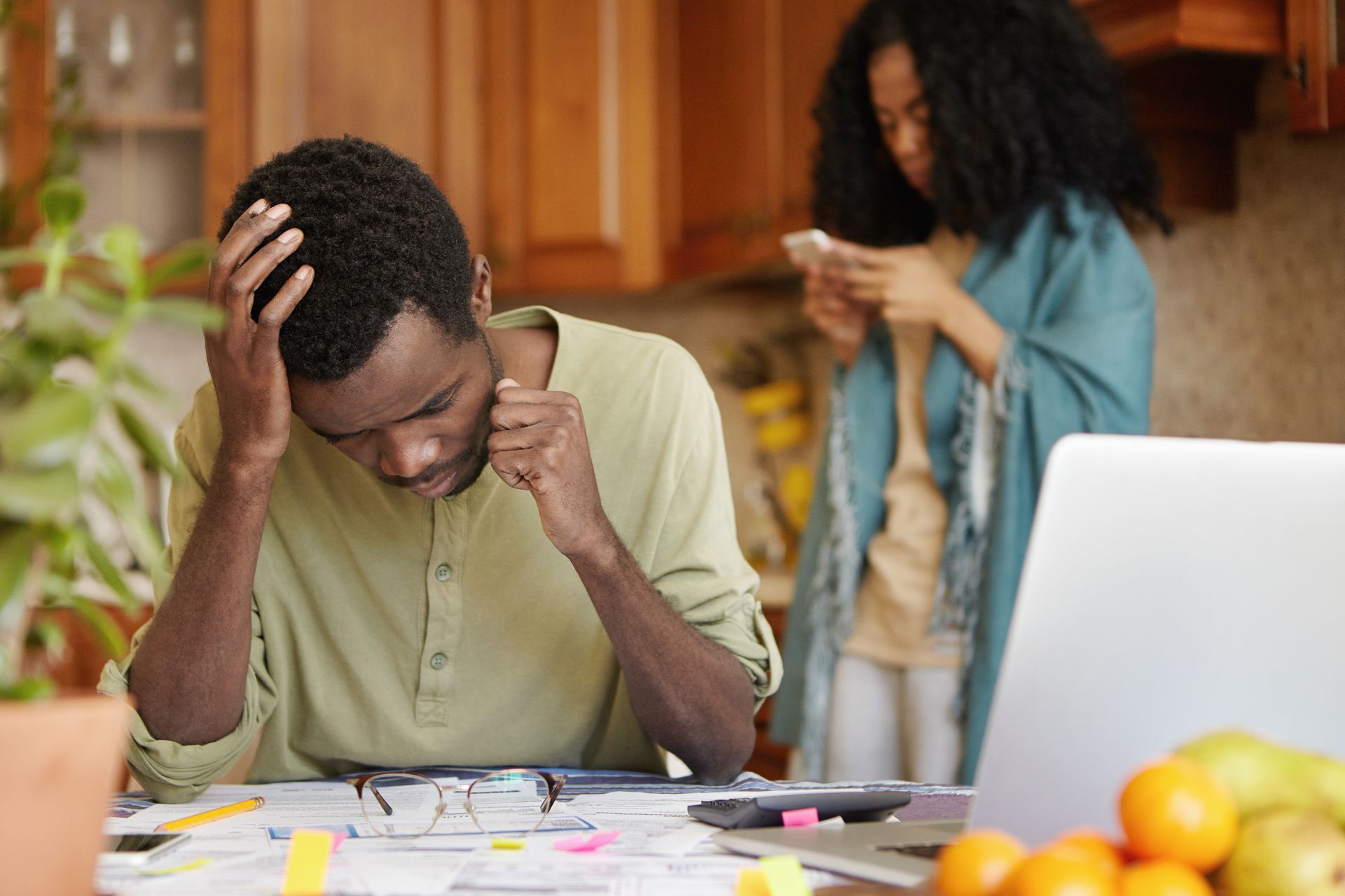 A stressed person holding their head with bills and a calculator on the table.