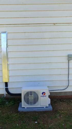 Exterior view of a white Gree air conditioner unit mounted on a concrete base next to a house wall.