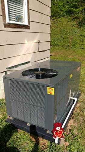 Air conditioning unit outside a building, gray and black with a fan on top.