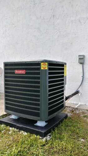 Goodman air conditioner unit outside against a white wall.