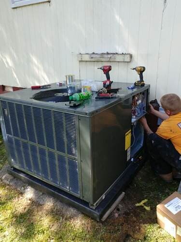 HVAC technician working on an air conditioning unit outside a building, with tools and components visible.