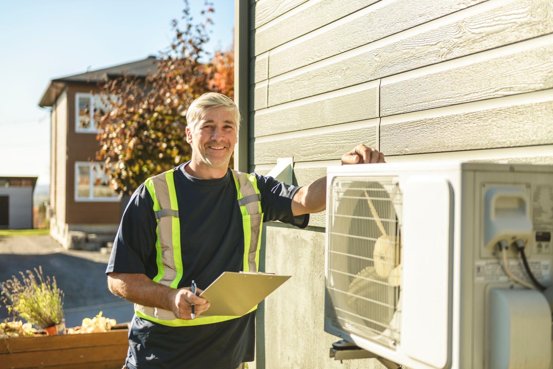 Technician with a clipboard inspecting an outdoor HVAC unit beside a house.