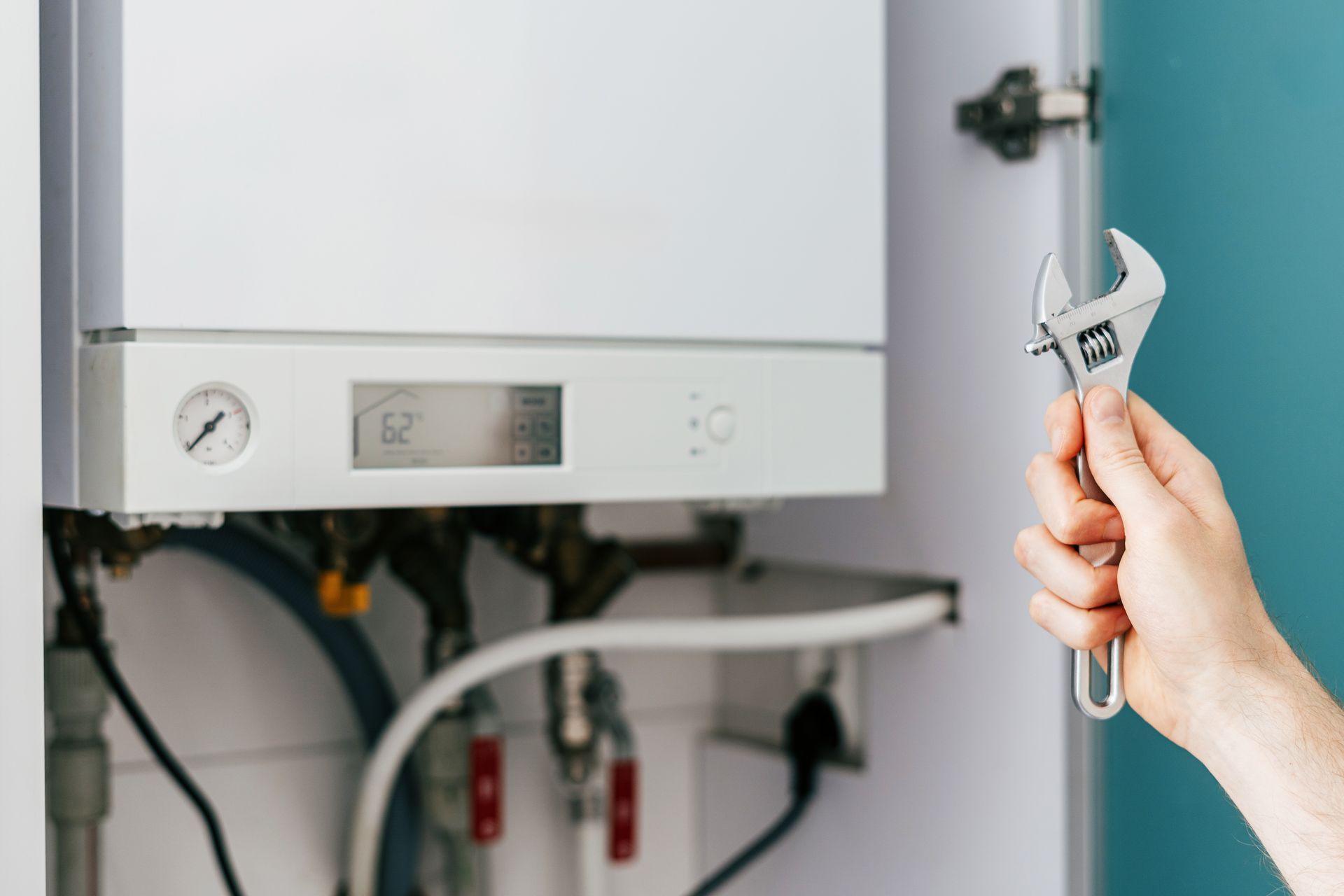 Hand holding an adjustable wrench next to a wall-mounted boiler during heating system maintenance.