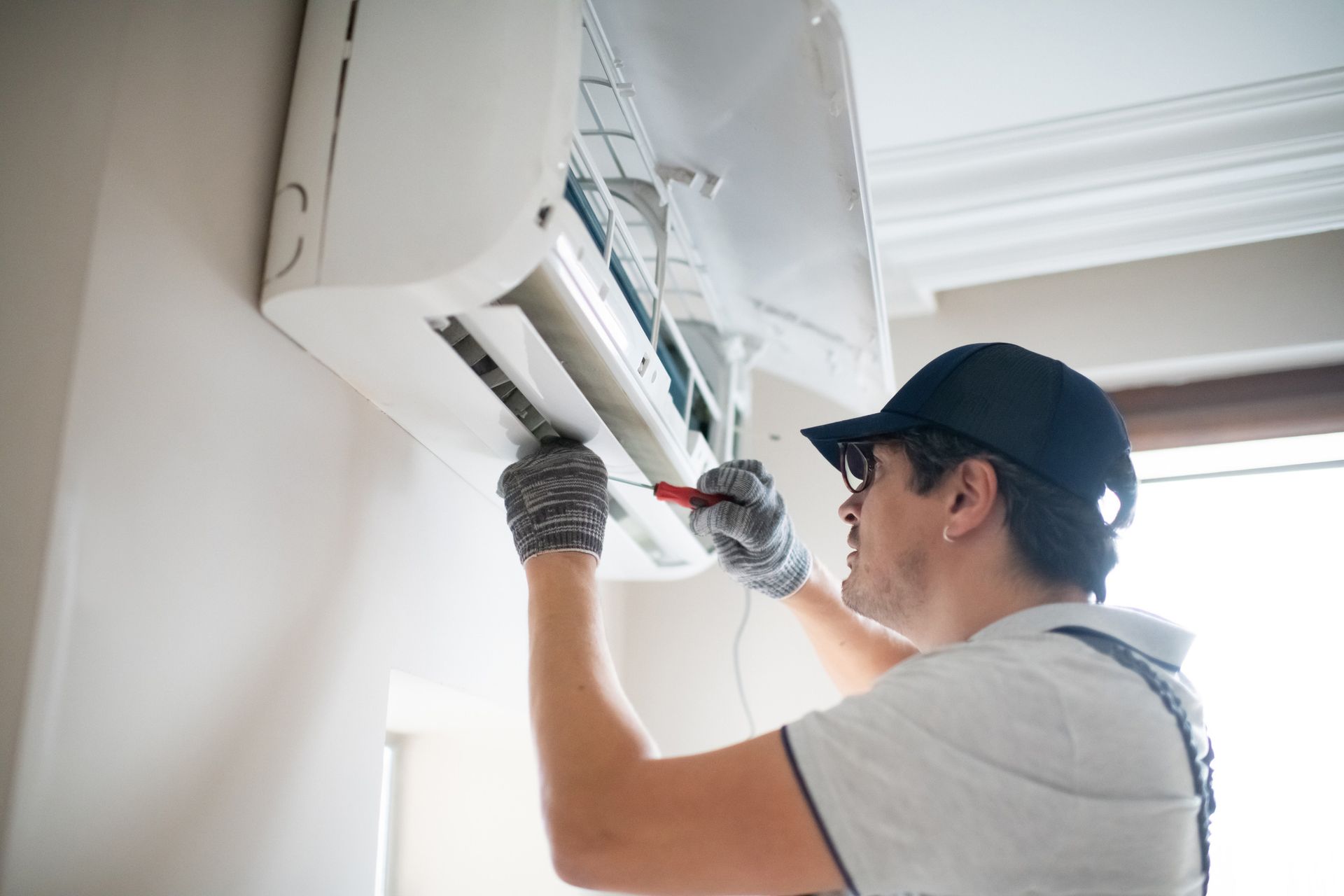 Technician repairing home air conditioner with screwdriver.