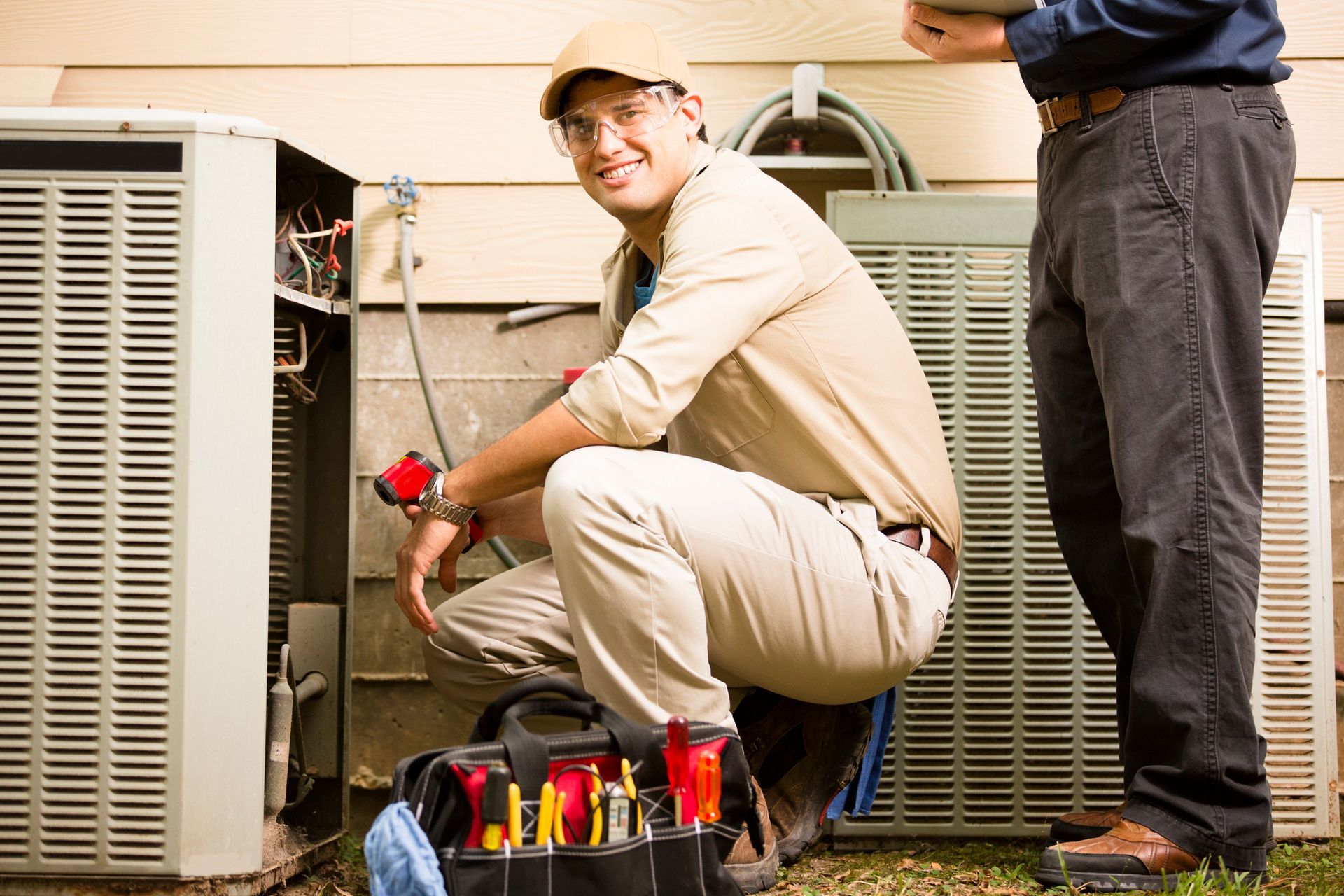 Two technicians in uniforms servicing an air conditioning unit with tools and a tablet.