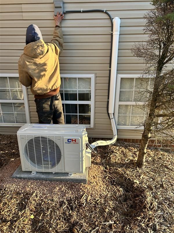 Man installing an outdoor air conditioning unit. He is reaching towards an electrical box on the house.
