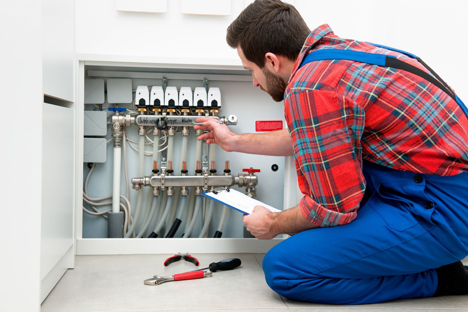 Plumber inspecting radiant floor heating manifold and zone valves during system installation.