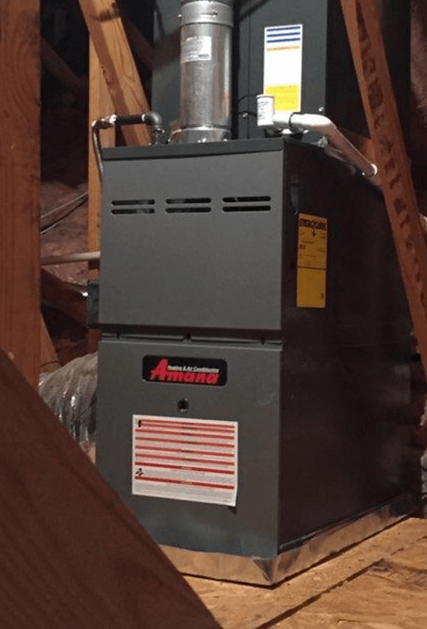 Gray Amana furnace in an attic setting, surrounded by wooden beams and ductwork.
