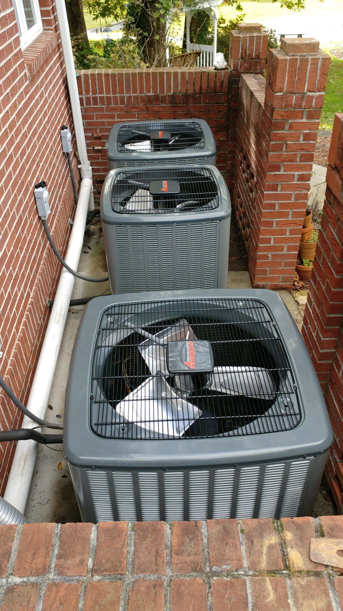 Three gray and black air conditioning units outside a brick building.