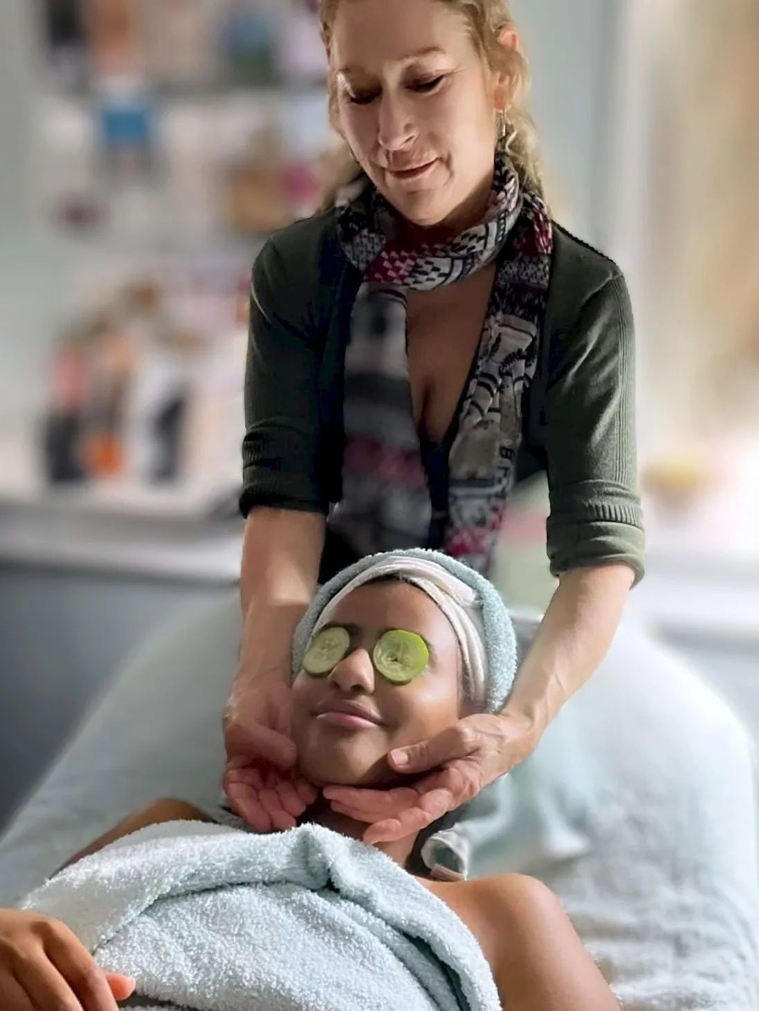 A woman is giving a woman a massage with cucumber slices on her eyes.