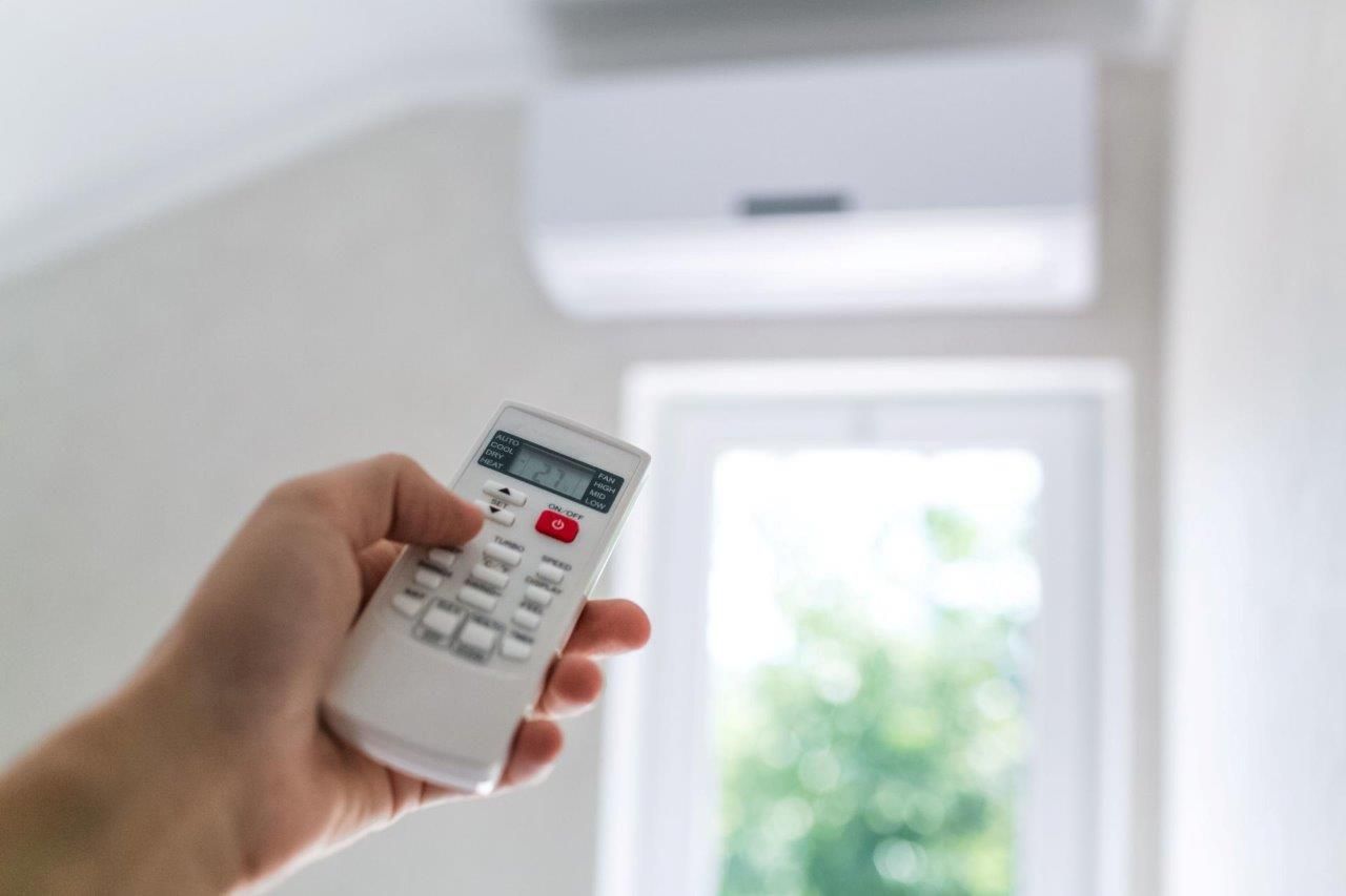 Una persona tiene in mano un telecomando davanti a un condizionatore.