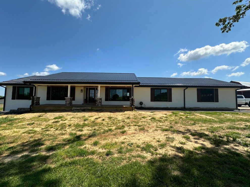 A large white house with a black roof is sitting on top of a lush green field.