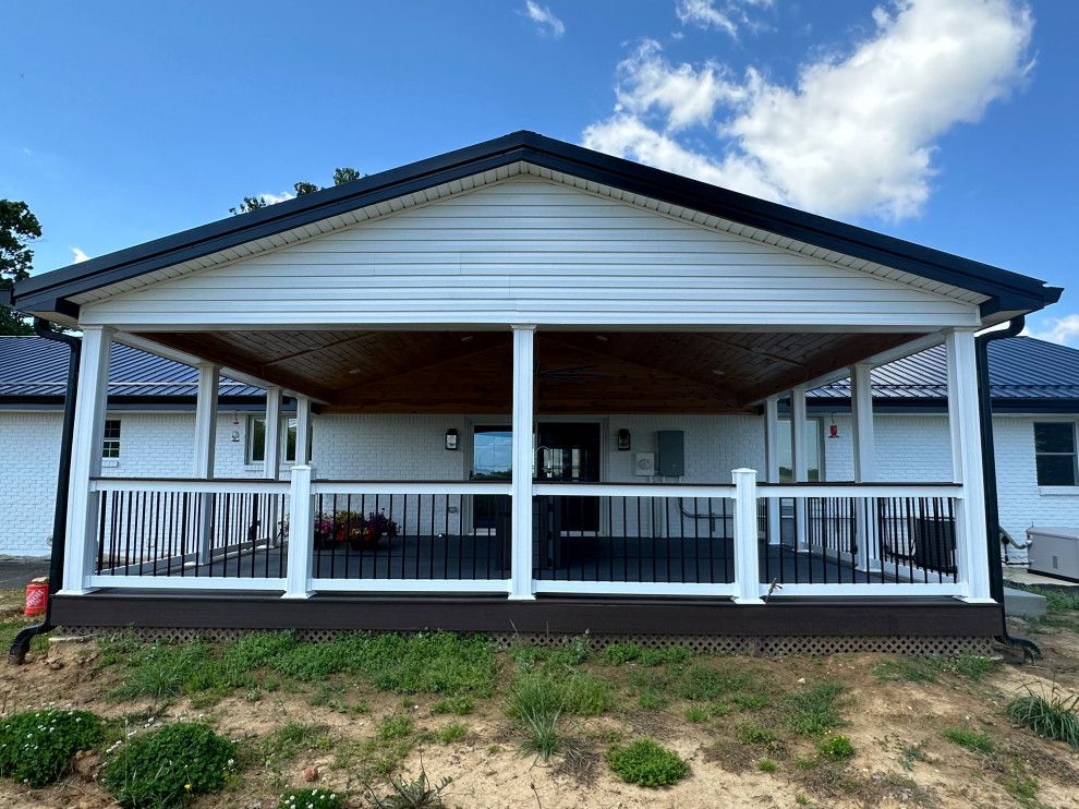 A white house with a large porch and a black roof.