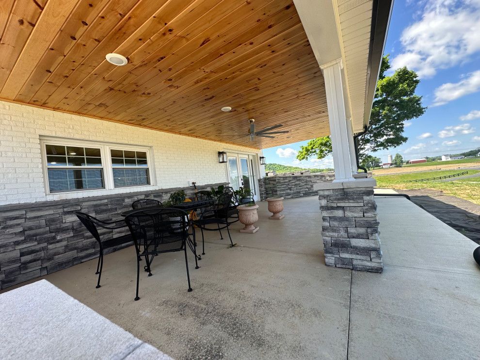 A porch with a table and chairs under a wooden ceiling.
