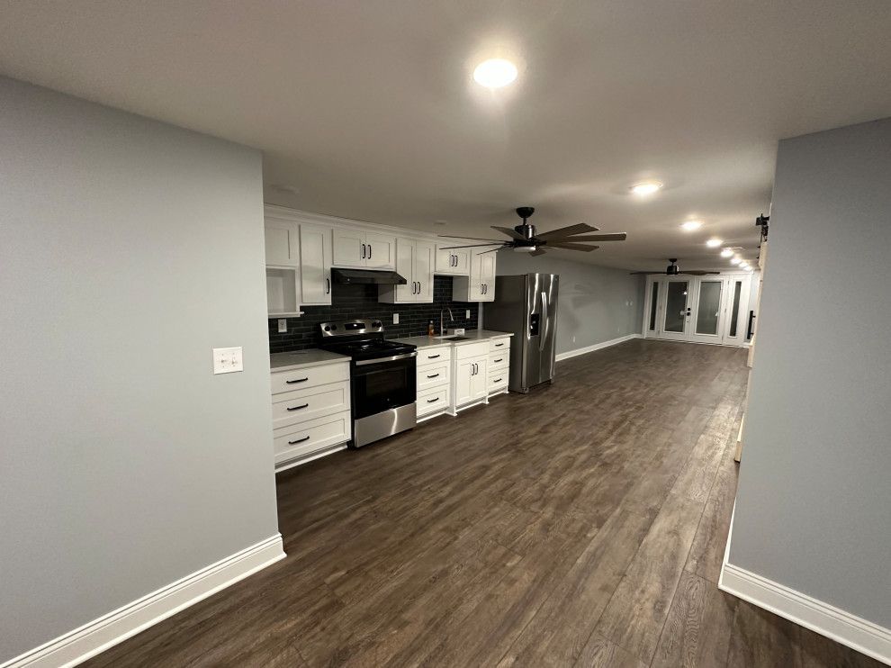 A large empty room with a kitchen and a ceiling fan.