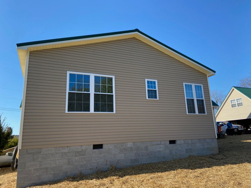 A house with a green roof and a lot of windows is sitting on top of a dirt field.