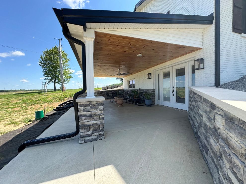 A large porch with a ceiling fan and a drainpipe on the side of a house.