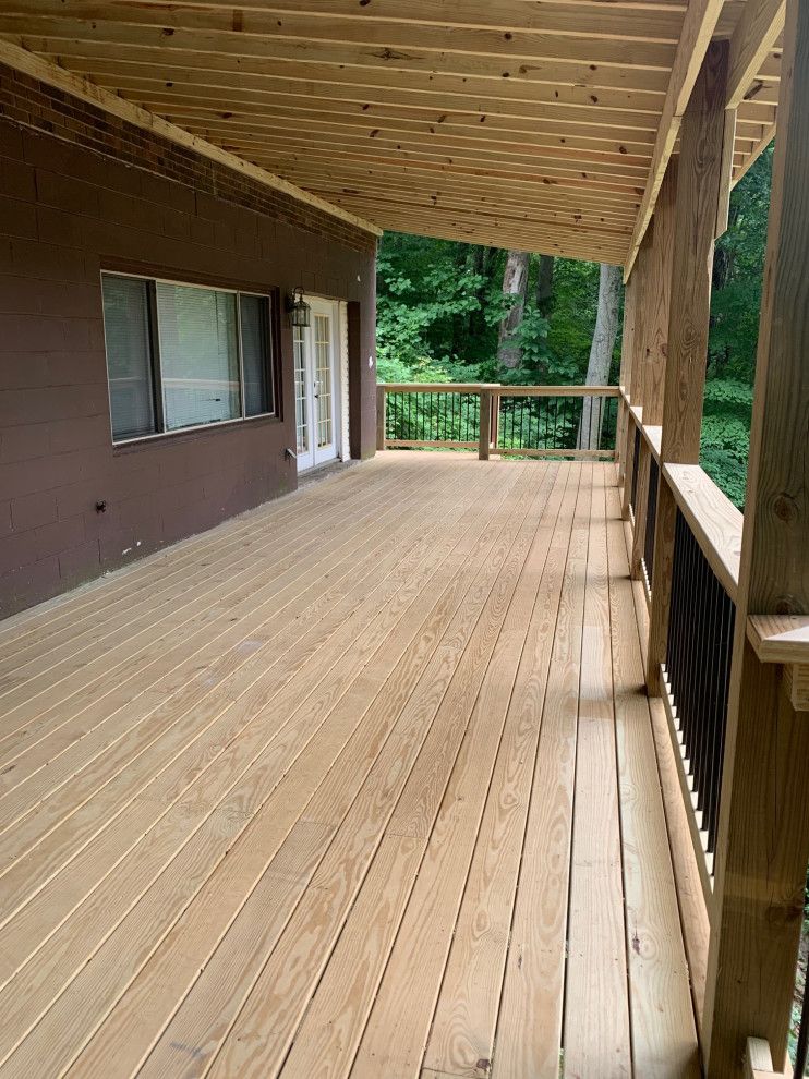 A large wooden deck with a covered roof in front of a house.